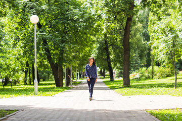 Beautiful young woman walking in green summer park