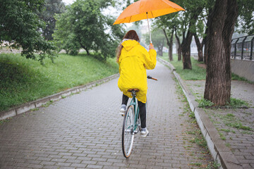 Fototapeta premium Rear view of bicycle rider wearing raincoat while cycling with umbrella