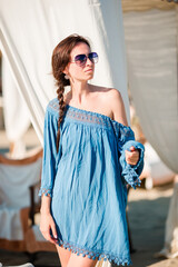 Young woman during tropical beach vacation. Fashion girl in white sunbeds at european beach weekeend