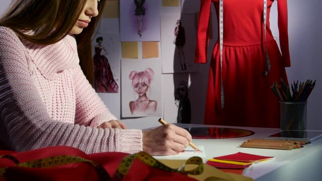 Designer draws a sketch in the background is a mannequin with a red dress. Close up