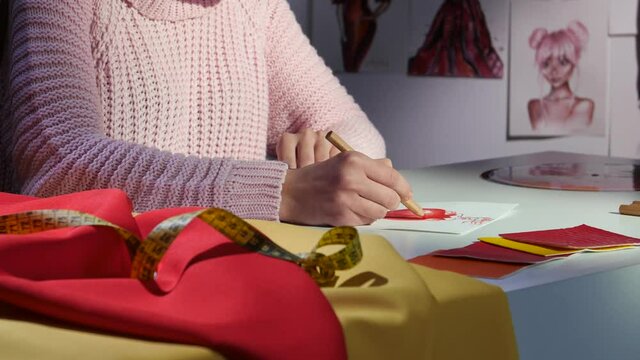 Designer's hands draw a sketch of a beautiful red dress. Close up