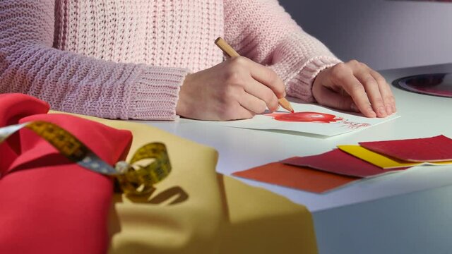 Hands designer draws a sketch of a dress, on a cloth table, for tailoring. Close up