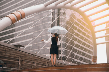 Thai pretty woman in black dress holding transparent umbrella walking on bridge crossing  landmark in Bangkok,Thailand.