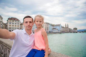 Fototapeta na wymiar Young dad and daughter taking selfie background famous Fraumunster Church and river Limmat, Switzerland.