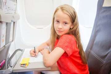 Adorable little girl traveling by an airplane. Kid drawing picture with colorful pencils sitting near window