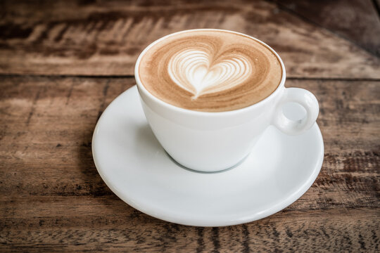 Drak tone filter,Close up white coffee cup with heart shape latte art on wood table at cafe