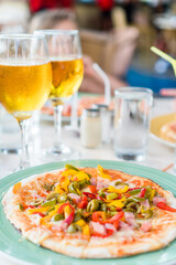 Pizza with mozzarella cheese, olive, fresh tomato and pesto sauce. Served at restaurant table with two beers