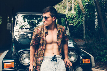 Handsome man traveling on by car in tropical forest at hot summer day. People traveling and tourism concept. © Nick Starichenko