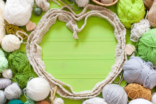 Knitted heart. Woolen yarn of natural shades on a green background.