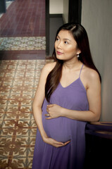 Fototapeta premium A pregnant woman wearing a purple dress indoors
