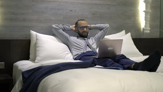 Happy businessman watching movie on laptop on bed in hotel room at night
