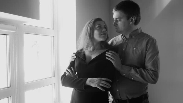 4K black and white video of beautiful couple kissing at big window