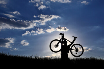 Fototapeta na wymiar silhouette of a cyclist with a raised bike in the grass in the sun.