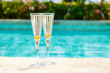 Two glasses of prosecco cocktail with orange berry at the edge of a resort pool. Concept of luxury vacation