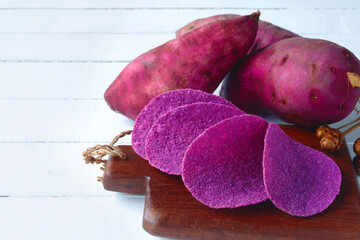 potato chips with raw sweet potatoes root in purple skin on wooden background