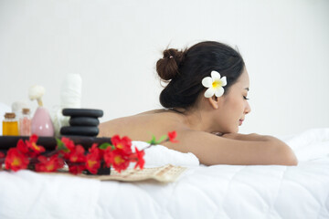 Obraz na płótnie Canvas Asian woman lay down on the bed in spa shop with stone flower and other equipment. Young woman in spa shop. Asian girl lay down on bed in spa with hot stone on back. Happy lifestyle concept.