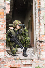 Portrait of armed woman with camouflage. Young female soldier observe with binoculars. Child soldier with gun in war, house ruins background.  Military, army people concept