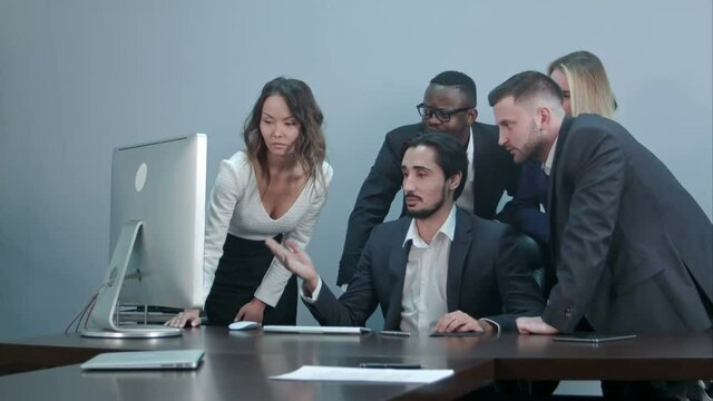 Group of multiracial business people around the conference table looking at laptop computer and talking to one another
