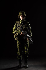 Portrait of armed woman with camouflage. Young female soldier observe with firearm. Child soldier with gun in war, black background.  Military, army people concept