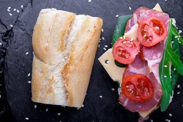 Open sandwich with jamon, arugula, tomatoes, cheese on stone slate black background. Top view