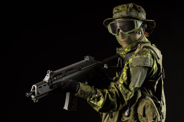 Portrait of armed woman with camouflage. Young female airsoft sniper observe with firearm. Soldier with gun in war, black background.  Military, army people concept