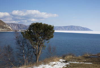 Baikal lake spring landscape view. Snow-covered shore of the lake. Rocky forested coastline. Boundary of ice and open water.