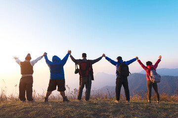 Group of four people stands on the top of mountain in winner pose. Team or teamwork success concept.Space for text. Travel concept. © tawanlubfah