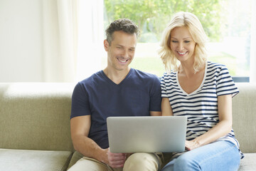 Browsing together. Shot of a happy mature couple relaxing on the couch using a laptop.