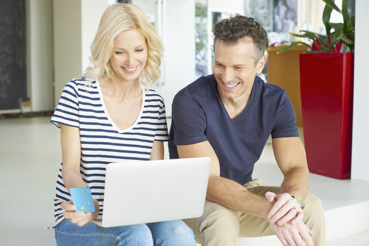Browsing together. Shot of a smiling middle aged couple sitting on couch and using credit card and laptop while shopping online. 