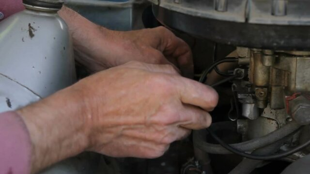 Old mechanic repairing an old car. Under the hood of the car checks the work of carb and engine