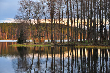 Fototapeta premium Wooden pavilion in the forest on the lake shore, reflecting in water
