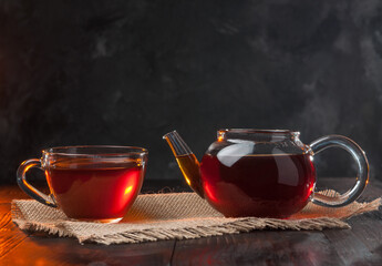 Tea ceremony,a Cup of freshly brewed black tea and glass teapot,warm soft light, darker background.