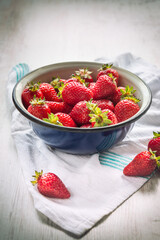 Close up of a blue metal bowl full of fresh strawberries over a white wood rustic background.