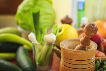 Wooden pestle and mortar surrounded with vegetables and fruit fresh from the market on a kitchen table