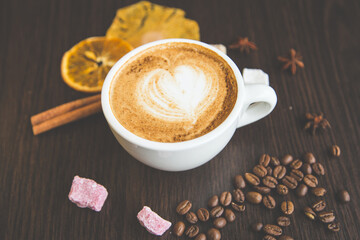 Top view of cappuccino hot coffee (or latte) in a white cup with latte art and roasted coffee beans, dried orange, cinnamon, sugar on wooden table background/ Instagram Filter