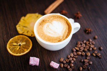 Top view of cappuccino hot coffee (or latte) in a white cup with latte art and roasted coffee beans, dried orange, cinnamon, sugar on wooden table background/ Instagram Filter