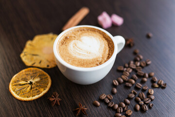 Top view of cappuccino hot coffee (or latte) in a white cup with latte art and roasted coffee beans, dried orange, cinnamon, sugar on wooden table background/ Instagram Filter
