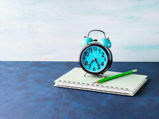 Alarm clock and businessman's accessories on blue background. Office manager morning concept with tie, notebook, stationery