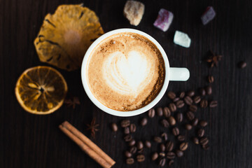 Top view of cappuccino hot coffee (or latte) in a white cup with latte art and roasted coffee beans, dried orange, cinnamon, sugar on wooden table background/ Instagram Filter