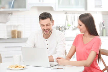 Young couple with laptop sitting at kitchen table