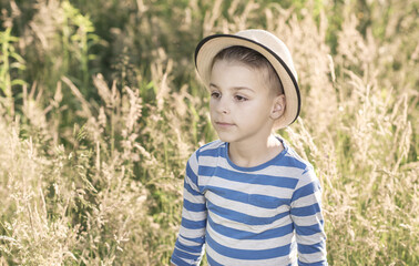 handsome boy stands in the grass field, a warm summer background behind him