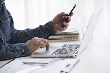 A businessman is using a laptop computer and a smartphone at the same time in the office