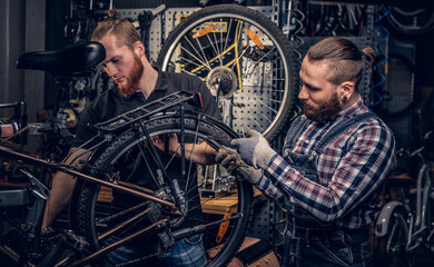 Two bearded mechanics fixing town bicycle in a workshop.