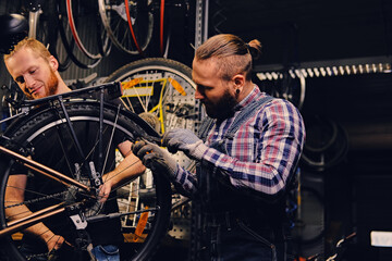 Obraz na płótnie Canvas Two bearded mechanics fixing town bicycle in a workshop.