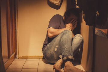 Man sitting in a corner, sad, depressed and lonely, crying