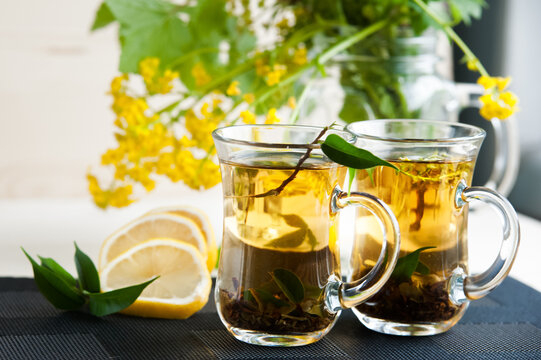 Two transparent cups with tea. Green, black, herbal, jasmine tea with lemon and ginger. Theme of tea. Cooking, tea packing, food production, restaurant business