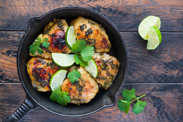 Homemade crispy cilantro lime chicken in a black cast-iron skillet on the rustic wooden table, top view. - 157374303