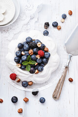 Pavlova - meringue cake with fresh berries on glass plate on old vintage white wood background. Top view, copy space.