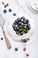 Pavlova - meringue cake with fresh berries on glass plate on old vintage white wood background. Top view, copy space.