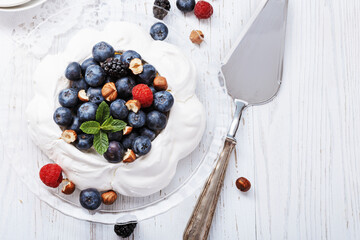 Pavlova - meringue cake with fresh berries on glass plate on old vintage white wood background. Top view, copy space.